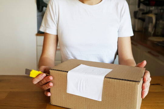 A photo of a parcel being unpacked in a cardboard box. A woman opens the box with her hands in Krakow, Poland, March. Delivery and packaging
