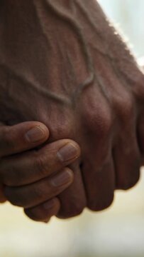 Vertical video: Clasping small hand wrapping large veiny hand near window, showing comfort