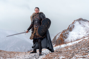 Rugged warrior stands poised with sword and shield against a backdrop of snowy peaks © horimono