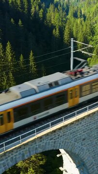 Vertical video: Camera tracking electric train crossing stone viaduct, pantograph passing catenary