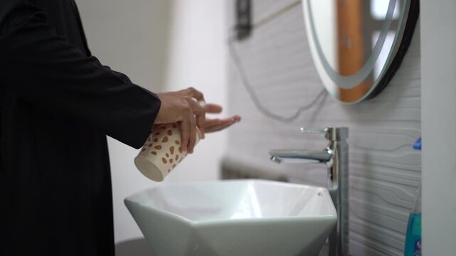 Close up of Muslim man hand wash in black Islamic Jubbah washing hands with liquid soap against white tiles background, hygiene and Wudu concept in 4k.