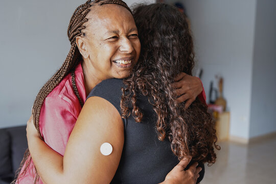 Happy african american mother hugging daugher with diabetes patch on arm at home - Family love, lifestyle and disease concept