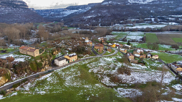 Aerial view of the small village of Arroyuelos, featuring green meadows dusted with light snow and surrounded by snow-capped mountains. Arroyuelos, Cantabria, Spain.