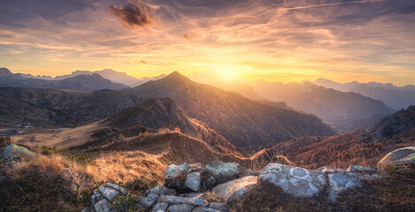 Fototapeta premium Stones and mountains at colorful sunset in autumn in Dolomites, Italy. Colorful landscape with rocks, mountain ridges, hills, orange grass and forest, golden sky with clouds in fall. Hiking. Nature