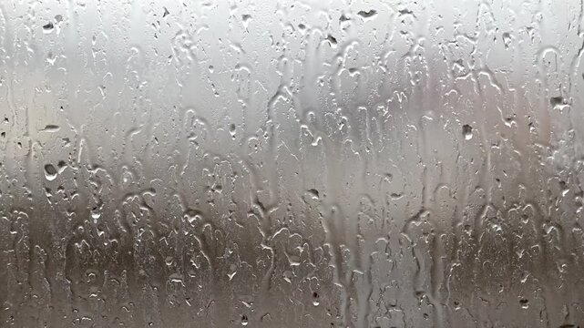 Raindrops slide down a fogged windowpane. Water beads cling, blur outdoor scenes. Mood feels calm, introspective, slightly melancholic. Perfect for scenes of solitude, reflection, or weather themes
