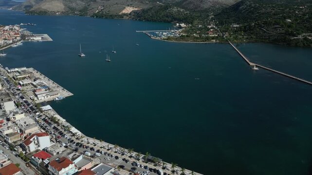 Aerial view of a coastal town with a marina, sailboats, and a long bridge stretching across a clear blue bay.