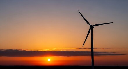 Obraz premium Silhouette of a wind turbine standing tall against a vibrant orange sunset with hues of blue and yellow in a serene landscape