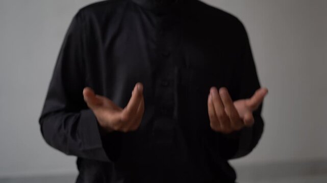 Close-up of Muslim man in black jubbah making questioning hands gesture and saying 'Why?', asking expression with natural light and white background in 4K.