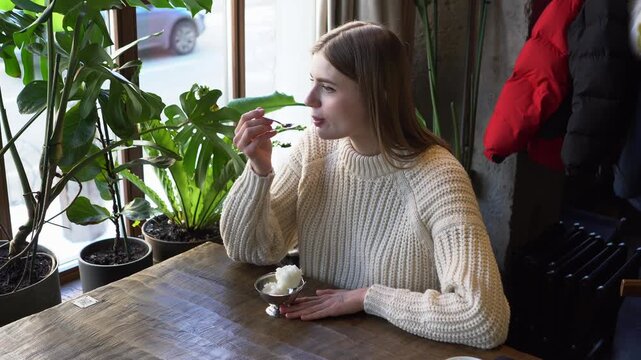 young beautiful woman eats ice cream with spoon in cafe, girl eats plombir dessert in restaurant