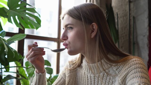 young beautiful woman eats borscht with spoon in cafe, girl eats soup with lard and bread in restaurant, close-up