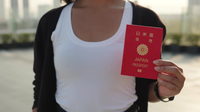 Woman hand shows passport of Japan citizen and stands on city street closeup. Lady demonstrates personal identification document on summer urban backdrop. Travel abroad preparation