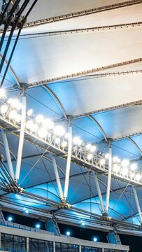 Vertical video: Camera panning, revealing tensile canopy in arena at night with lights and cables