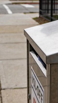 Adult hand reaching then inserting two envelopes into stainless-steel drop box to mail letters