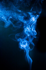 Obraz premium Mysterious blue smoke gracefully swirls against a dark background, creating a mesmerizing visual. The smoke takes on elegant, cloud-like forms, evoking a sense of calm and wonder.