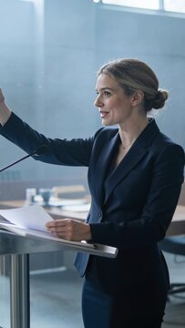 Speaking woman in navy suit delivering remarks at hearing room, holding papers by metal podium mic