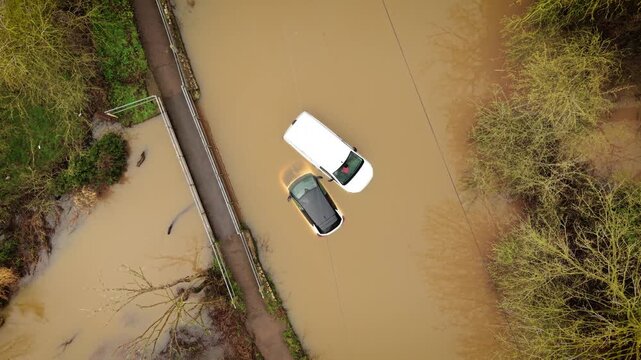 Climate change flooding submerging cars on countryside road after torrential rain. Extreme rainfall creating deep muddy water and trapping vehicles near rural bridge. Natural disaster impact bringing