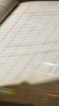 Vertical video: Tilting camera revealing ledger pad on desk, showing shifting streaks and blue grid