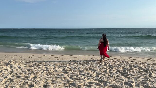 Woman in red dress walking along sandy beach shoreline in Rio de Janeiro Brazil enjoy peaceful lock down camera full bod