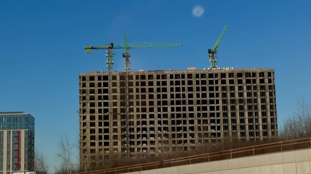 Construction of a massive connected residential block in Moscow Salaryevo Park. Large concrete building frames and multiple cranes against a blue sky. Modern urban housing development and city growth.