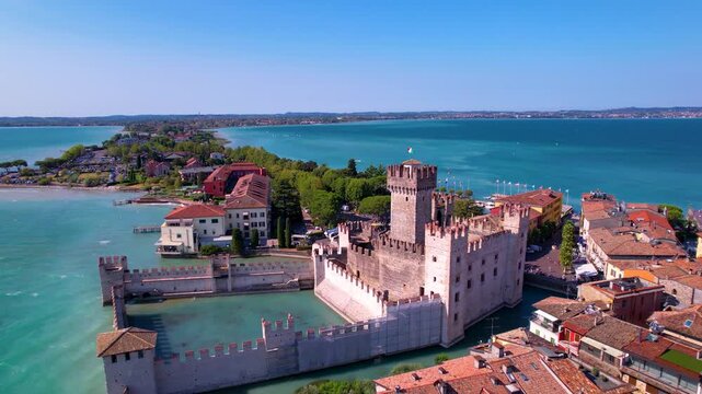 Italy Sirmione aerial drone fly-out reveal of medieval Scaliger Castle and long narrow peninsula in Lake Garda. Turquoise lagoon water and authentic old town scenery Lombardy North Italy travel 4k