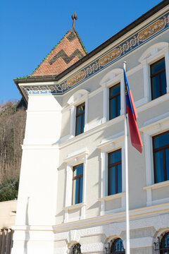 View of the Liechtenstein flag fluttering proudly against the backdrop of an ornate building with a tower under a clear blue sky, Vaduz, Vaduz, Liechtenstein.