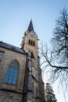 View of the towering spire of St. Florin Cathedral rises against the pale blue sky, framed by stark, bare branches, a contrast of stone and nature, Vaduz, Vaduz, Liechtenstein.