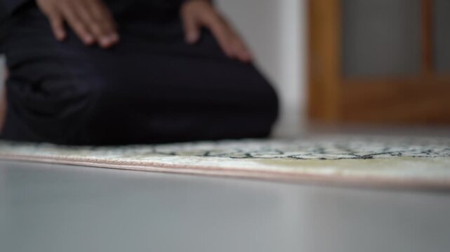 4K Close up of Muslim man in black jubbah rising from Sujud to sitting position on prayer mat, performing Salah, Islamic prayer ritual concept.