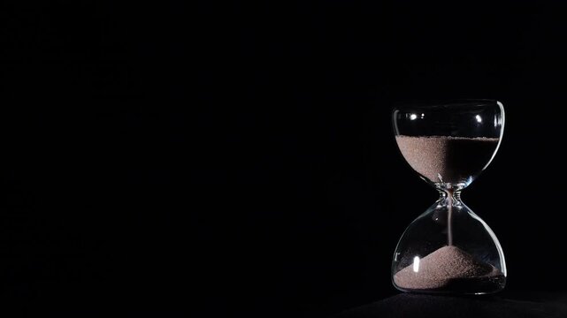 Hourglass flowing on black background. Right align comp with copy space on top and left, time management concept, minimalist product shot, hourglass in motion, clean style, approaching end

