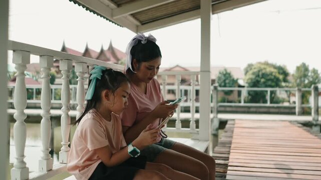 Mother and daughter using smartphones together on a pier ignoring each other