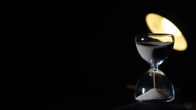 3 minute hourglass steady flow on black background. Soft yellow reading lamp bokeh behind upper glass, right aligned with extreme copy space, cinematic low light, 3 min sand timer
