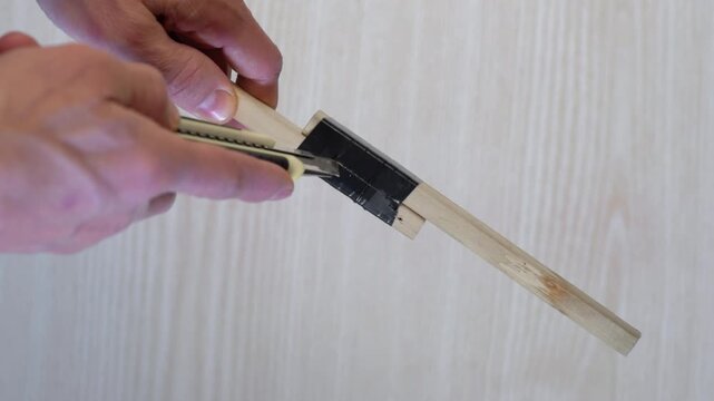 Removing tape carefully. Carefully peeling off electrical tape from wooden connection with knife. Employing utility knife to detach adhesive tape from wooden dowel joint on table