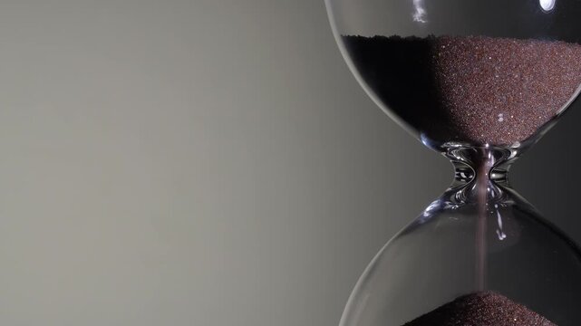 Macro of sand pile rising in hourglass neck on white background. Close up of sandglass finishing flow, left copy space, time is up concept, deadline approaching, minimalist product shot