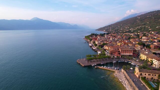 Lake Garda Torri del Benaco aerial drone pullback castle and marina reveal sunset luxury travel destination Italy scenic medieval harbor village 4K cinematic footage