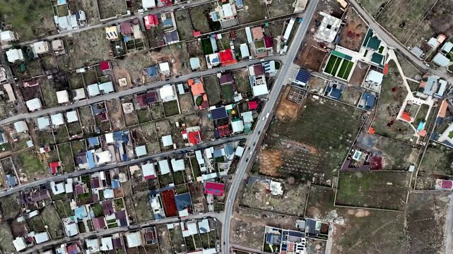 Aerial view of suburban neighborhood with colorful houses. Roads divide residential plots with green spaces. No people visible in frame