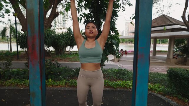Young Asian woman doing a leg curl exercise hanging from a bar in the park