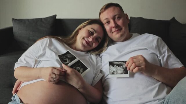 Pregnant woman and man sitting on floor holding ultrasound images. They smile happily while anticipating their new baby. Ideal for parenting, family planning, and pregnancy related content.