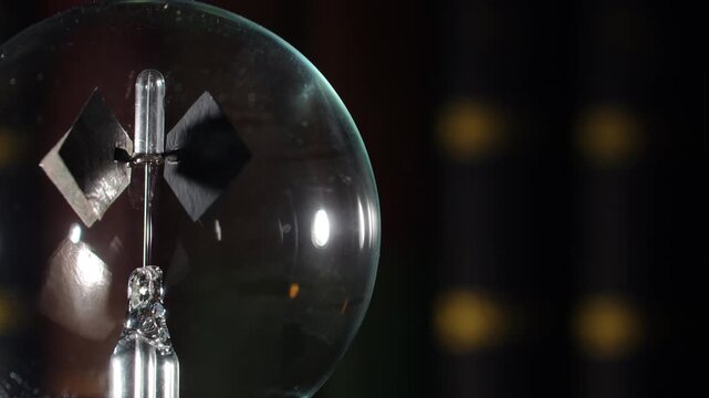 Extreme close up macro of rotating left align Crookes radiometer light mill with gold reflections on bookshelf background, start-stop motion, cinematic warm lighting, left copy space