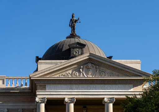 A historic courthouse in Georgetown, Texas features a statue on its dome against a clear blue sky. Blindfolded Justice statue on dome.
