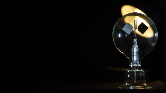 Rotating Crookes radiometer light mill with warm backlighting on black background. Right aligned composition with copy space, physics experiment, solar vane, cinematic lighting, start-stop motion