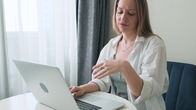 Woman suffering wrist pain while working on laptop at home, feel discomfort after prolonged typing. Remote work strain, repetitive injury and digital lifestyle health risks from overuse