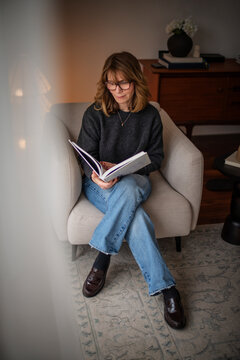 Blond haired woman in casual clothes with a book in her hand relaxing at home