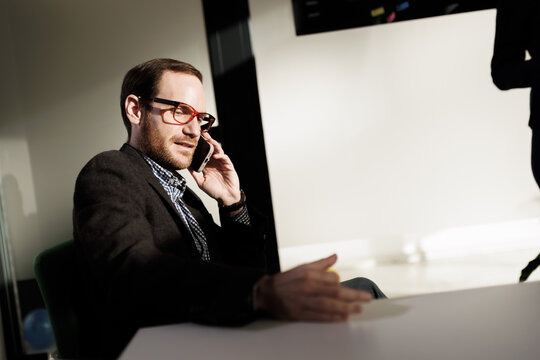 Businessperson engaged in a phone call while sitting at a table in a modern office during the daytime
