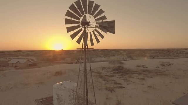 Aerial Drone Views Over Monahans Sandhills State Park Texas at Golden Sunset Showing a windmill in the sunset.