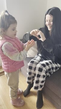 Older sisters showing heart sign with hands while little sister tries to copy but fails