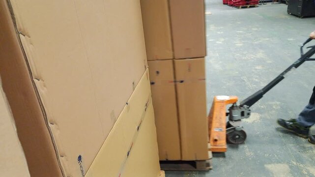 Caption: A skilled worker uses a manual pallet jack to move finished wooden cabinets, neatly stacked on a pallet, to the shipment area.