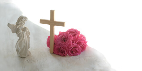 Naklejka premium Easter holiday background. Beautiful angel figurine with wooden cross and pink rose flowers on light table close up. symbol of Easter, Christianity religion, faith in God, prayer, memory. copy space