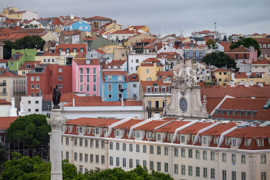 Rossio Square column and baroque facade amid colorful pastel buildings and terracotta rooftops covering the hillside of Lisbon's Baixa and Mouraria neighborhoods