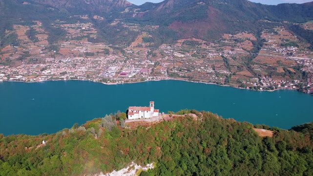 Italy Lake Iseo Monte Isola aerial drone tilt down to Santuario della Ceriola church on ridge. Scenic mountain peak and emerald water view. Underrated hidden gems Italian lake travel scenery 4K