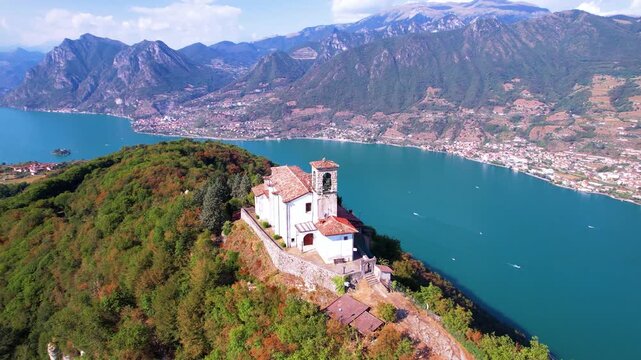 Italy Lake Iseo Monte Isola aerial drone orbit of Santuario della Ceriola church on mountain peak. Scenic 360 panorama of underrated Italian lake and Alps mountains. Lombardy travel scenery 4k