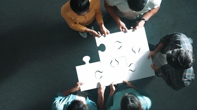 Top down view of business people put last piece of jigsaw puzzle together to complete puzzle and standing while wearing casual cloth. Group of diverse team finding solution with teamwork. Symposium.